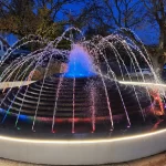 Sunbury fountain at night with lights colouring the water.