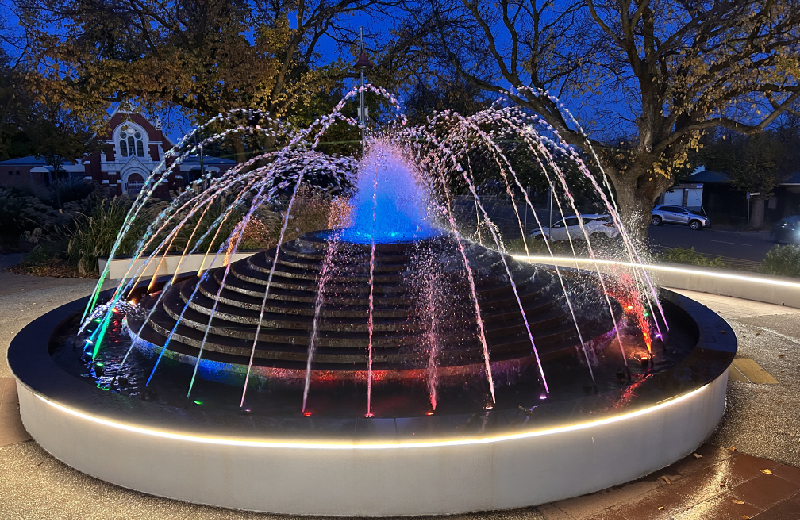 Sunbury fountain at night with lights colouring the water.